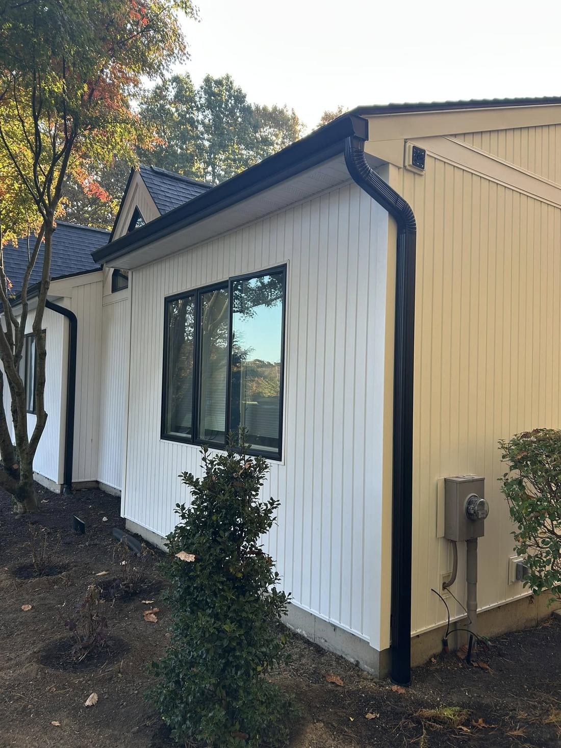 Black seamless gutter and downspout installed along white board-and-batten siding