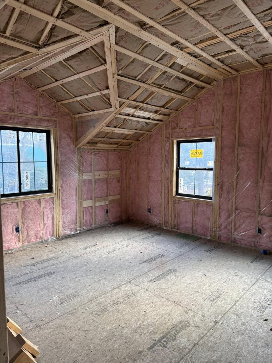 Unfaced pink fiberglass insulation fitted into 2 by 6 wall cavities and ceiling bays of a new Rhode Island home
